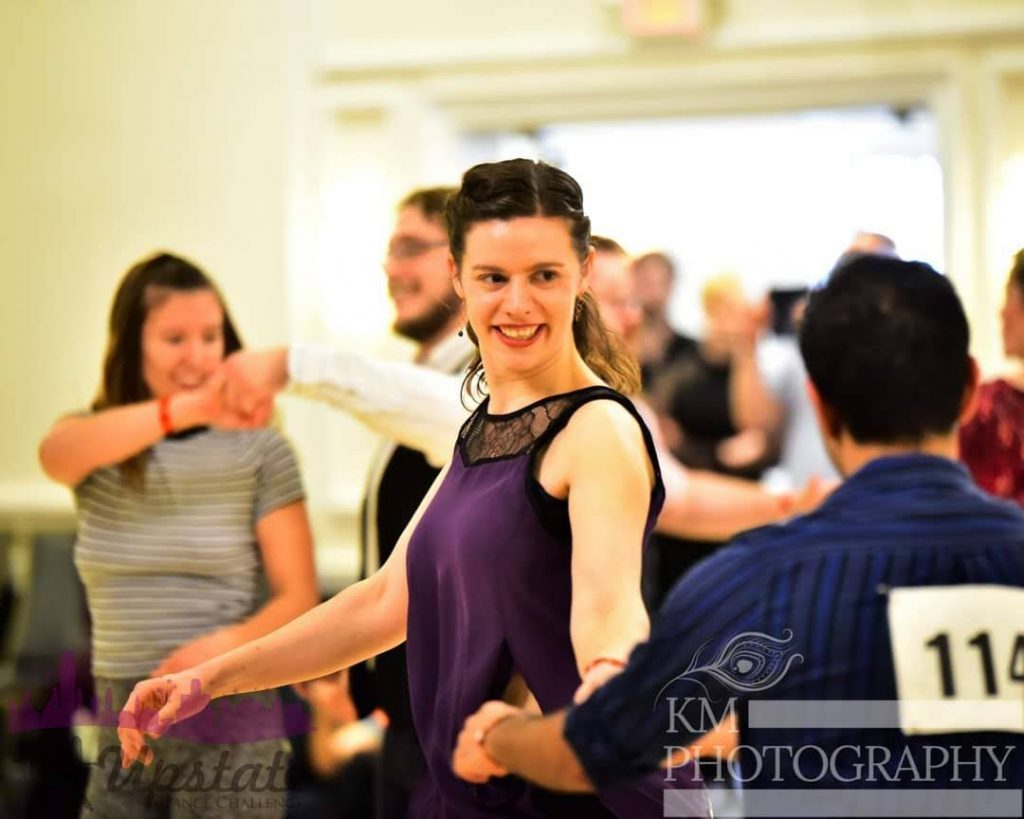 Woman in a purple shirt dancing in a West Coast Swing competition.